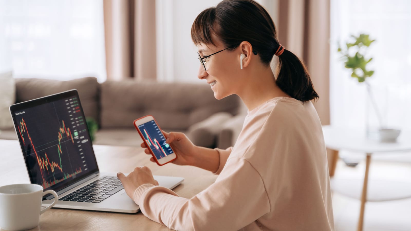 A smiling woman looking at her investment graphs on both her computer and cell phone to represent Vanguard's Total Market Index Funds.