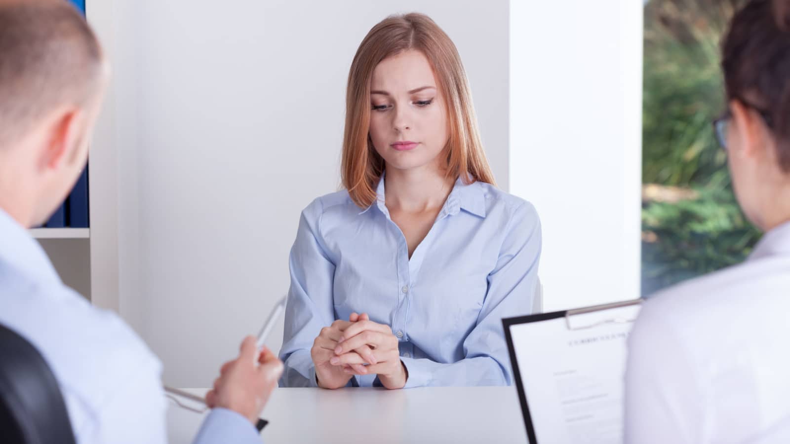 A woman looks uncomfortable as she sits at a financing table to represent cosigning a loan. The image represents the question "why is cosigning a loan a bad idea?"
