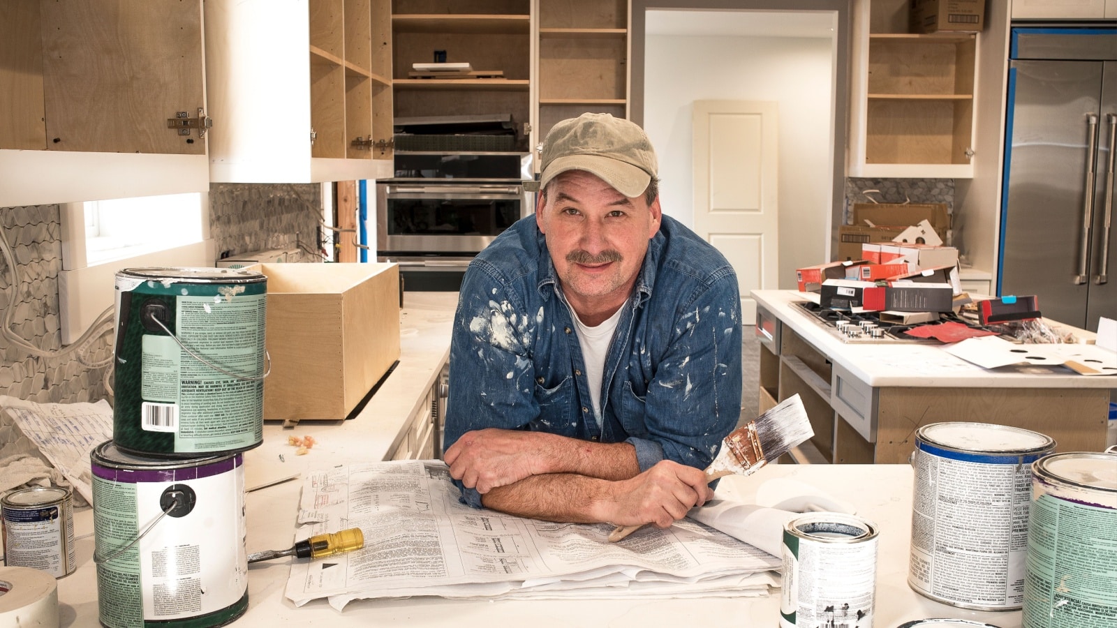 A painter standing in the kitchen of a home in the middle of a renovation project to represent buying a fixer upper.