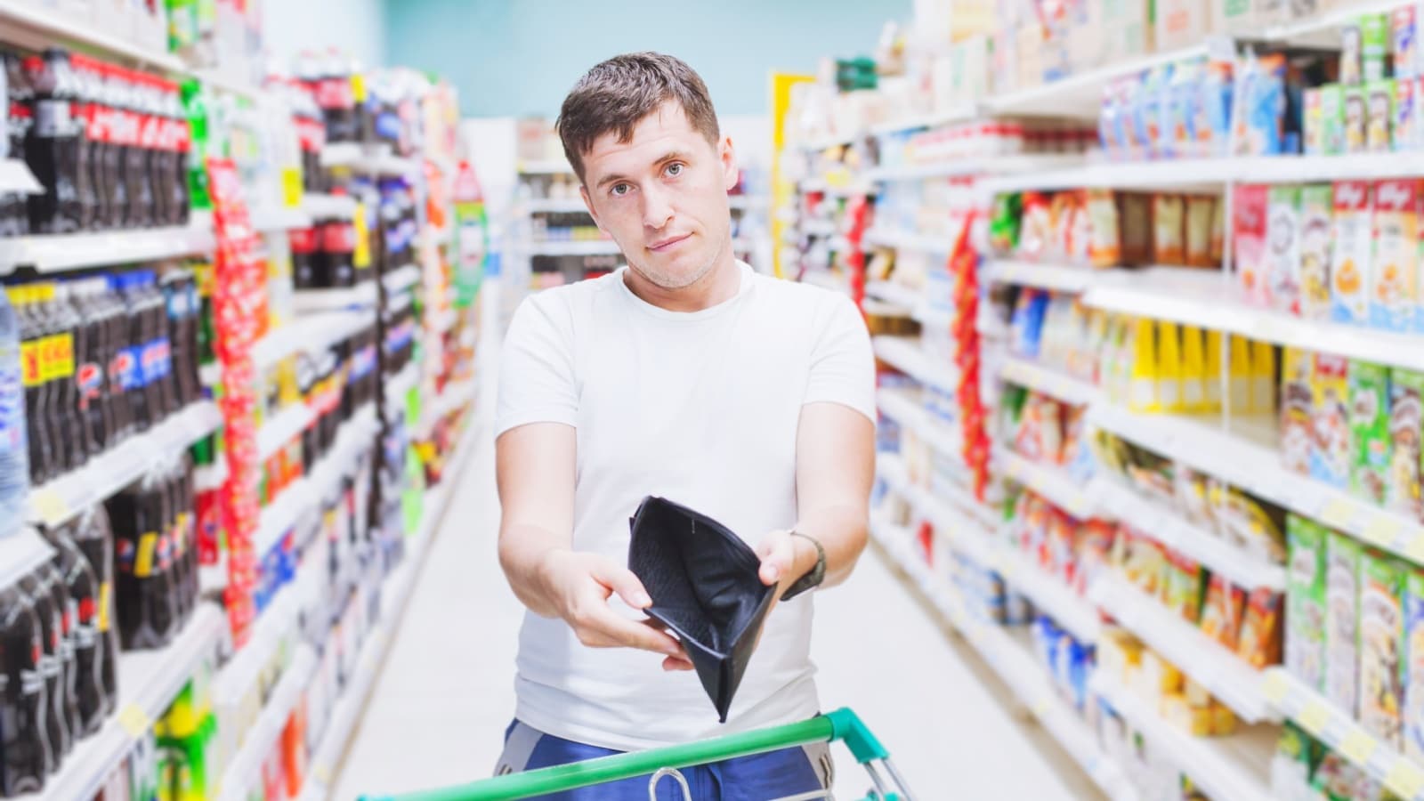 A man holds open his empty wallet in a grocery store to represent a $20 grocery budget.