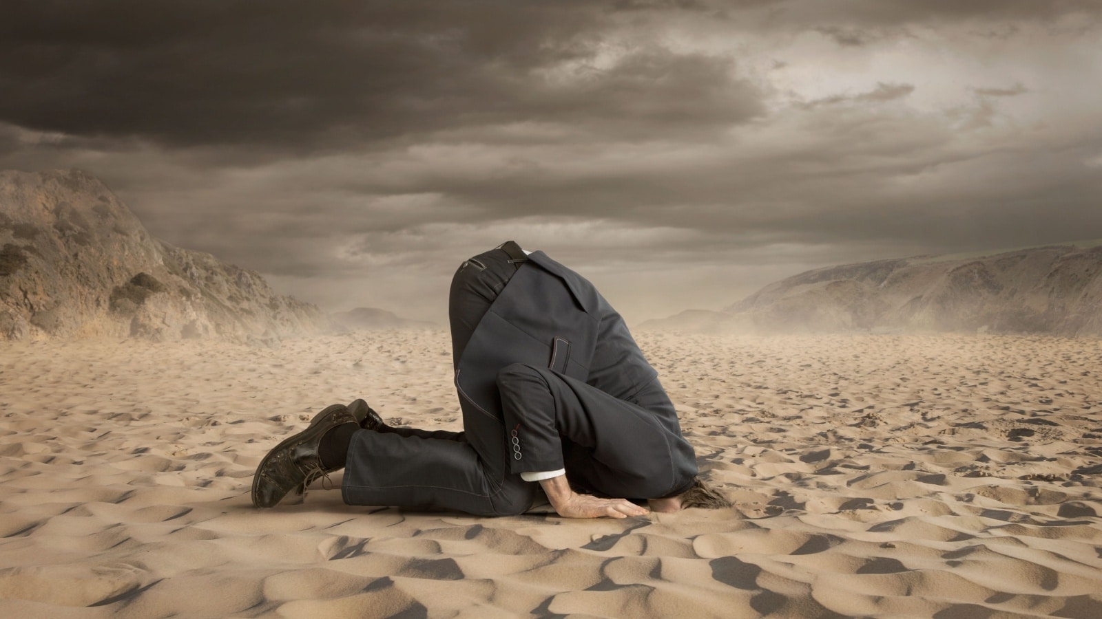 A business man with his head buried in the sand to represent someone who ignores money problems.