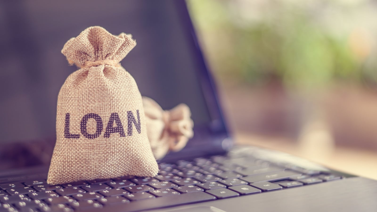 A money bag labeled "loan" resting on a laptop keyboard to represent peer-to-peer lending.