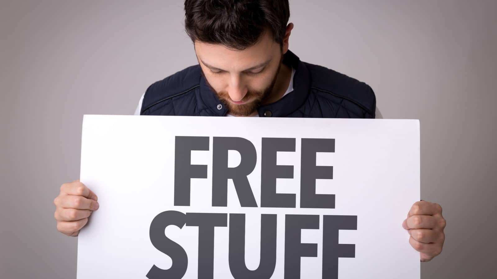Man holding a sign that says "free stuff." He's looking down at the writing to represent the idea that nothing in life is free because you are the product.