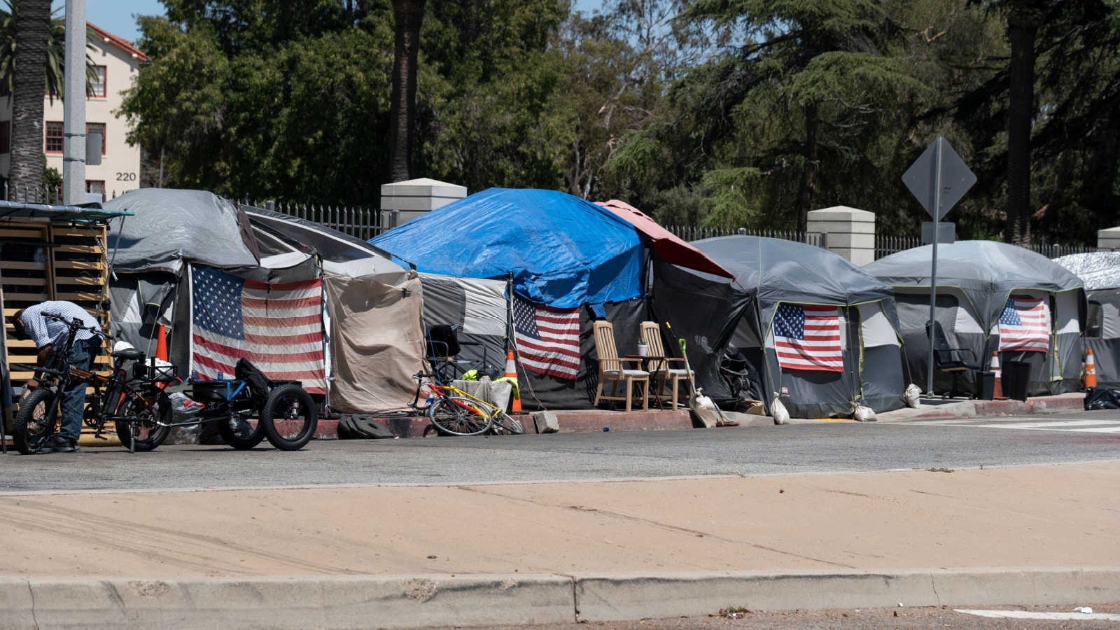 A shanty town of tents line a street in Los Angeles. US flags appear on the front of many tents. The scene represents America's poverty trap.