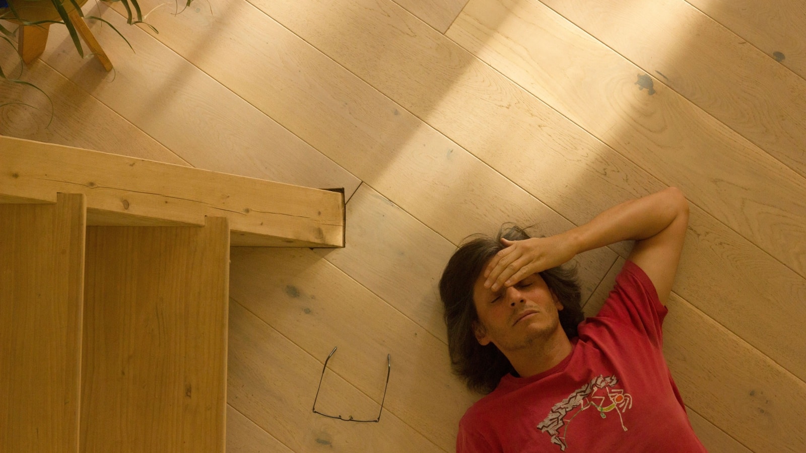 A stressed man feels like he doesn't belong. He lays on the floor with his hand on his head and glasses to the side, representing imposter syndrome.