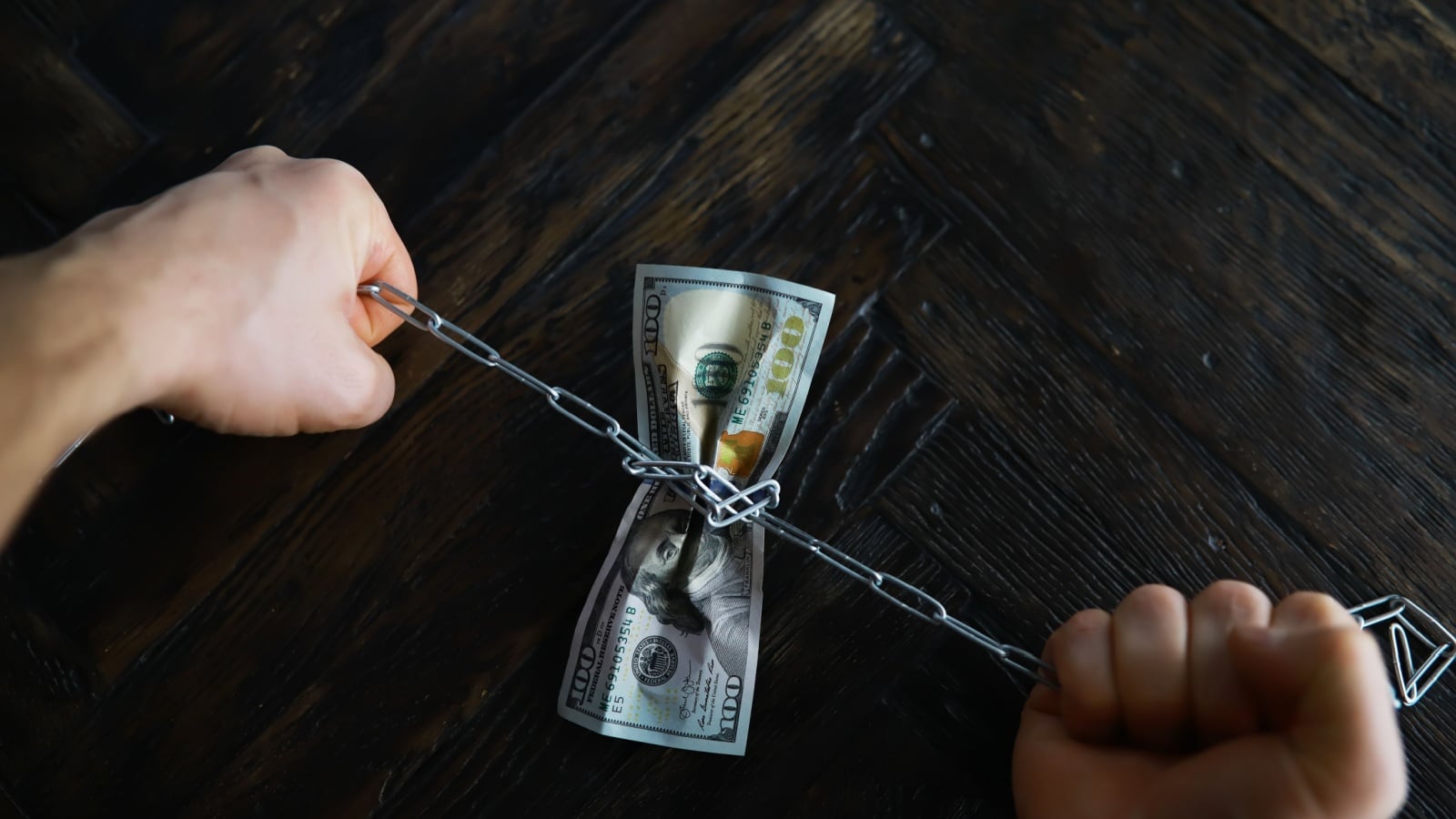Hands tightening a chain around a $100 bill to represent the scarcity mindset.
