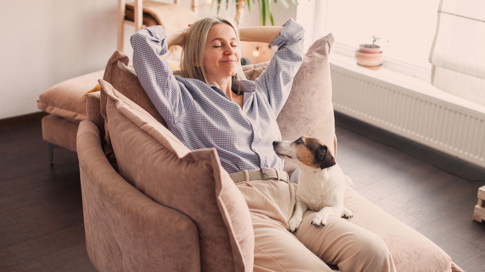 A woman enjoying a staycation. She's relaxing in a comfy chair with her dog on her lap.