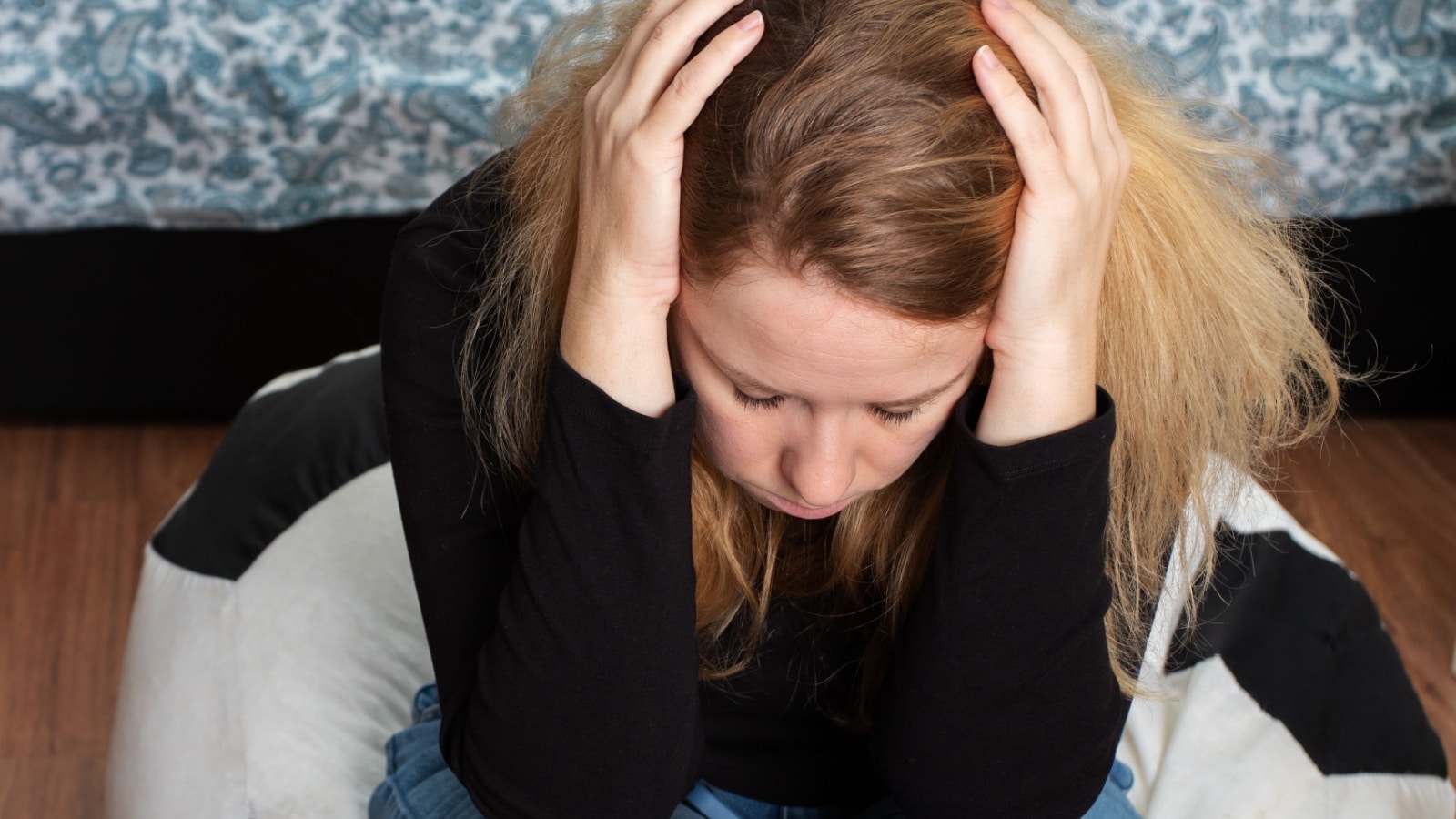 An anguished woman sitting with her head in her hands to represent financial abuse.
