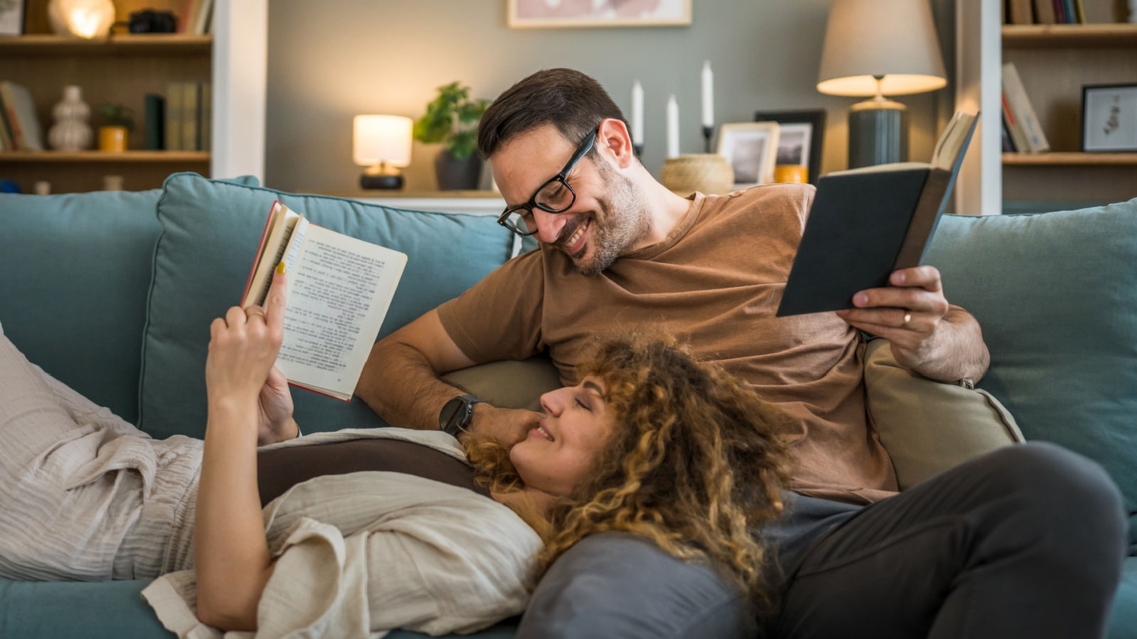 A happy couple on the couch reading and cuddling together. The photo represents how to live a rich life without a lot of money.