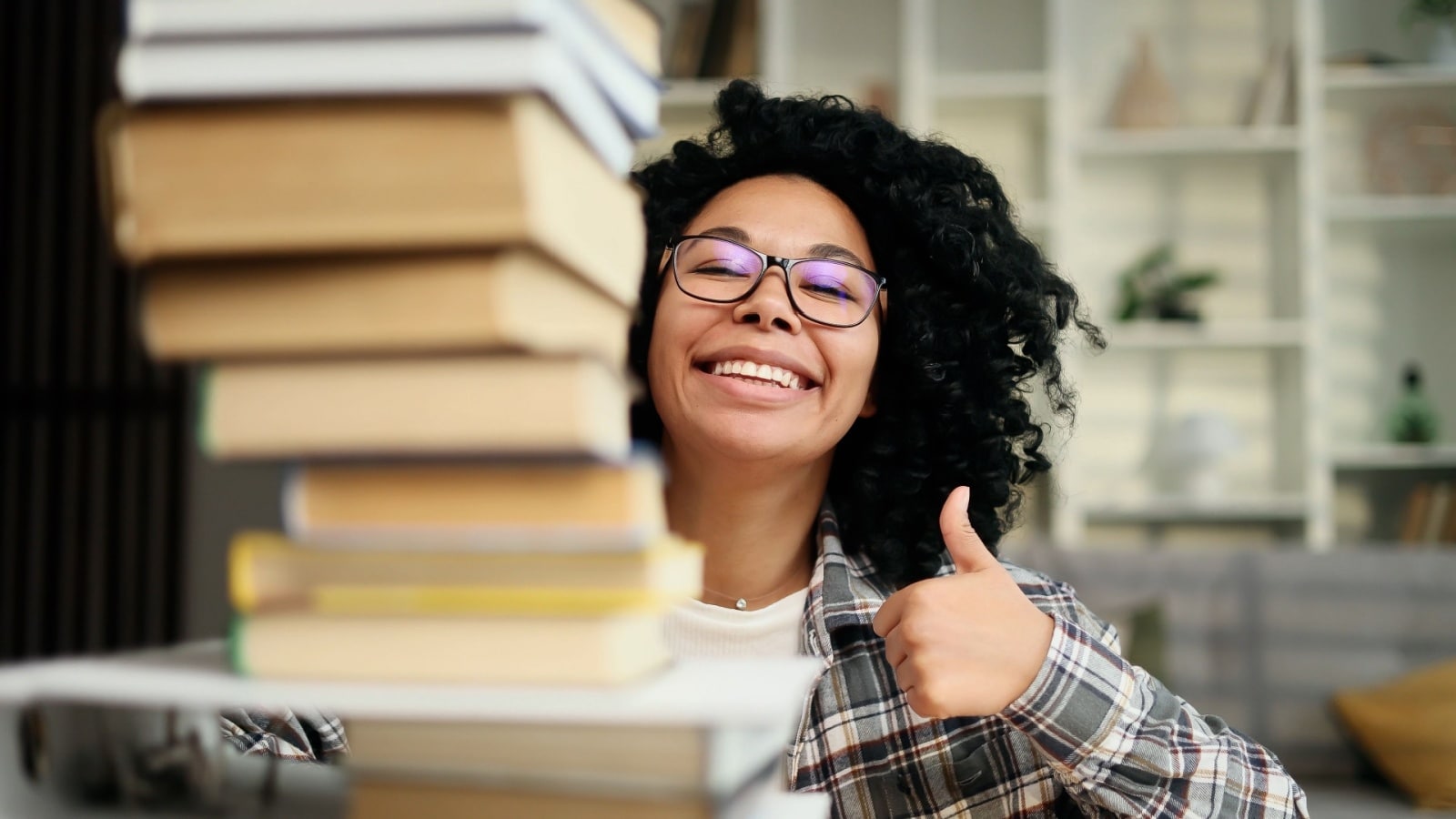 A smiling woman caring a stack of books to represent books for productivity.