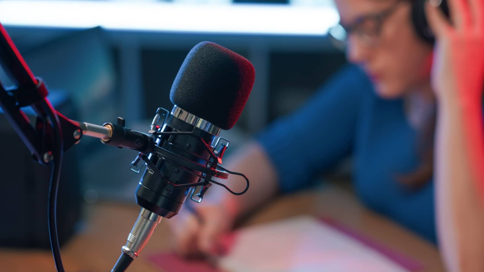 A broadcasting microphone in the foreground with a blurred production worker in the background to represent broadcasting lessons.
