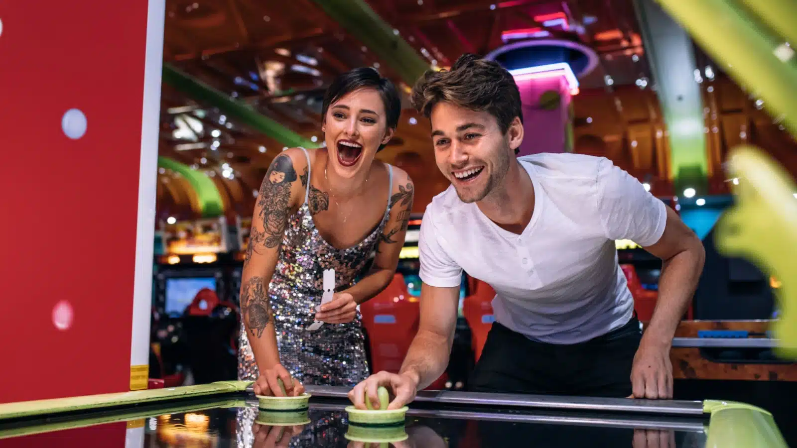 A couple plays air hockey at an arcade. 