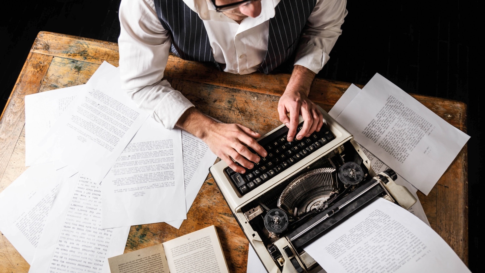 A man writing at a typewriter surrounded by papers to represent creative writing prompts.