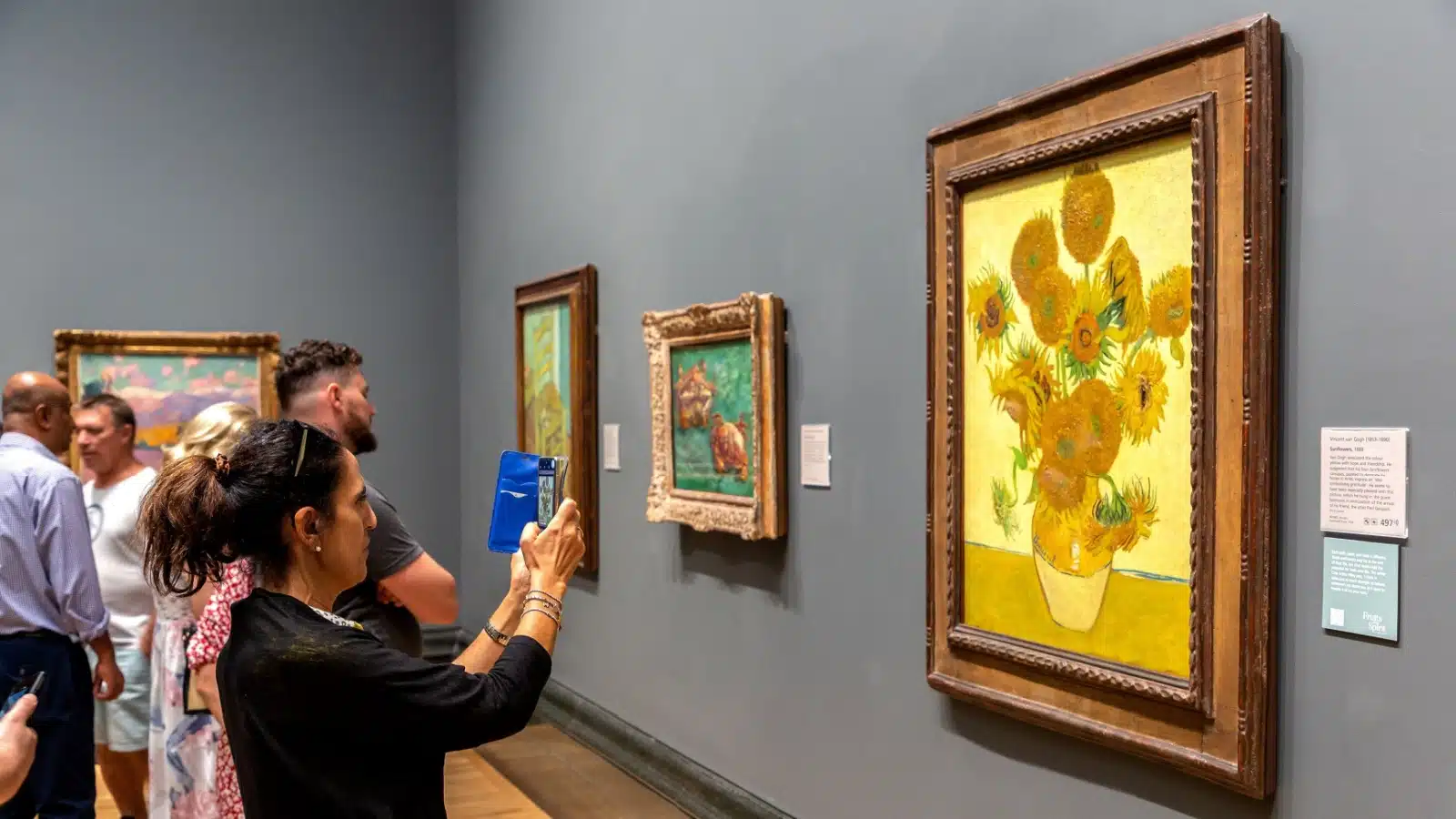 Van Gogh's Sunflowers painting hangs in a gallery in London while crowds admire it. 