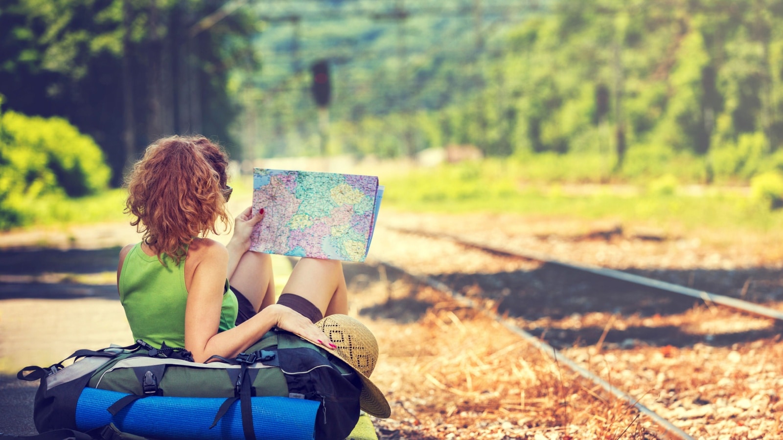 A woman traveling alone. She's resting by a railroad track with her luggage, looking at a map, to represent solo travel.