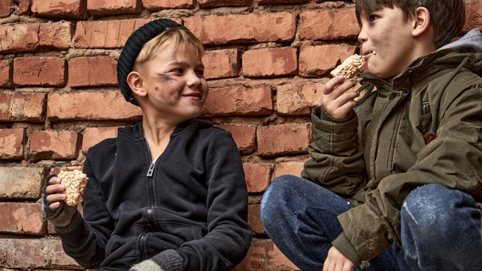 A pair of homeless street kids smile while enjoying a meal together. The photo represents children living in generational poverty.