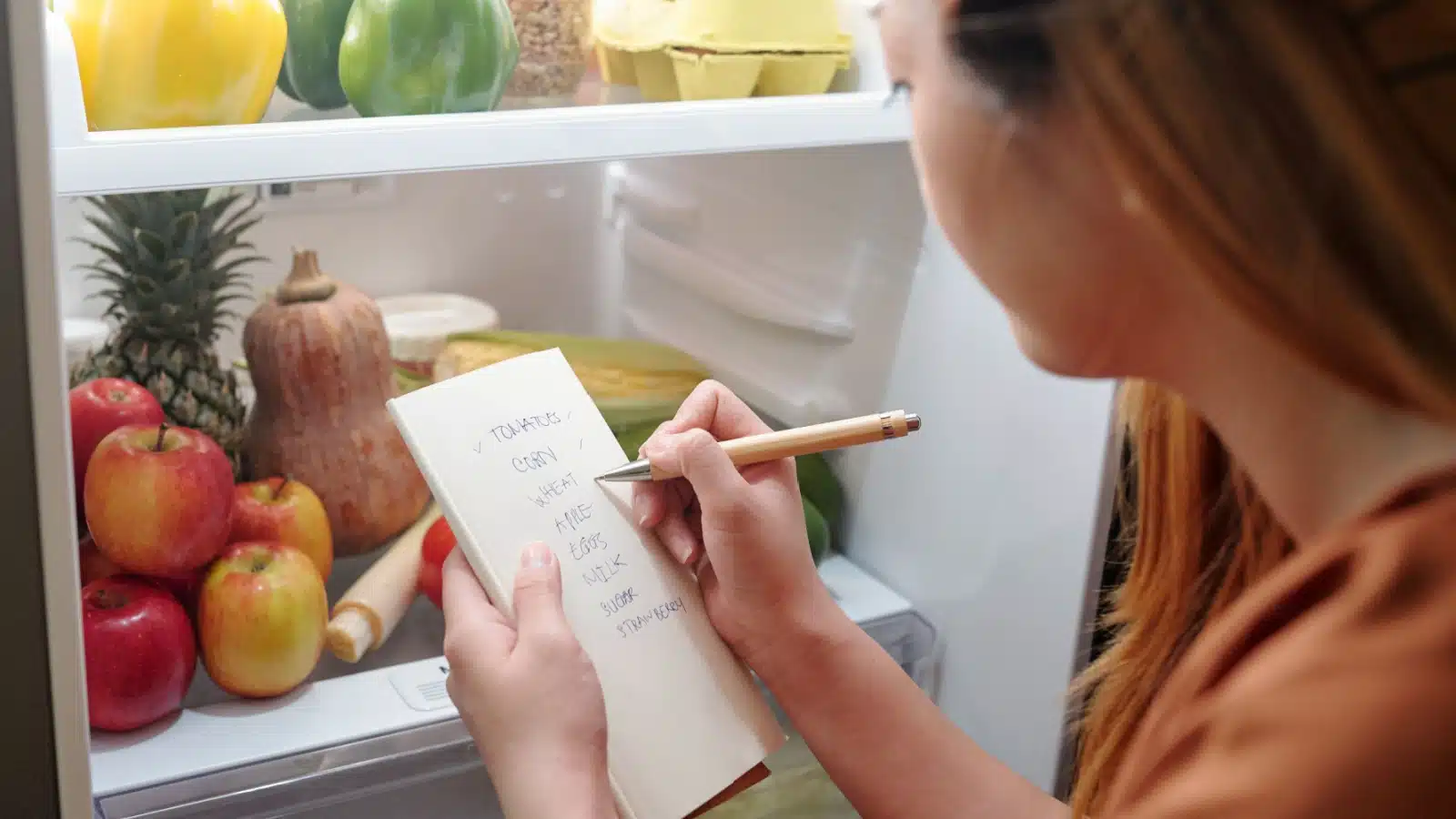 A woman looks in her fridge as she makes her grocery list.