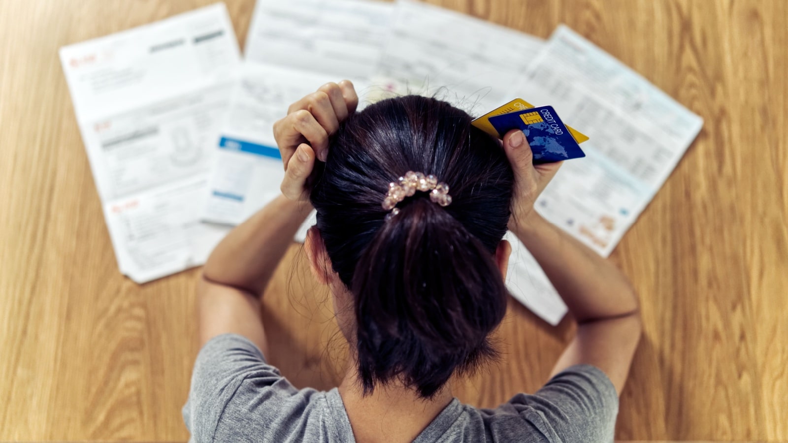 Top view of a stressed woman holding her head with credit cards in her hands, looking down at the bills to represent someone who is hemorrhaging money.