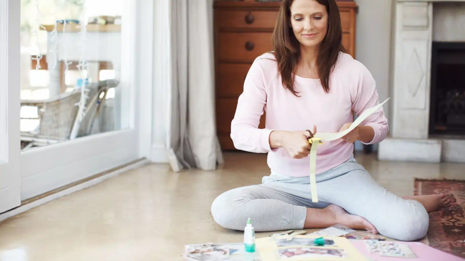 A woman sits on the floor cutting paper for an art journal. 