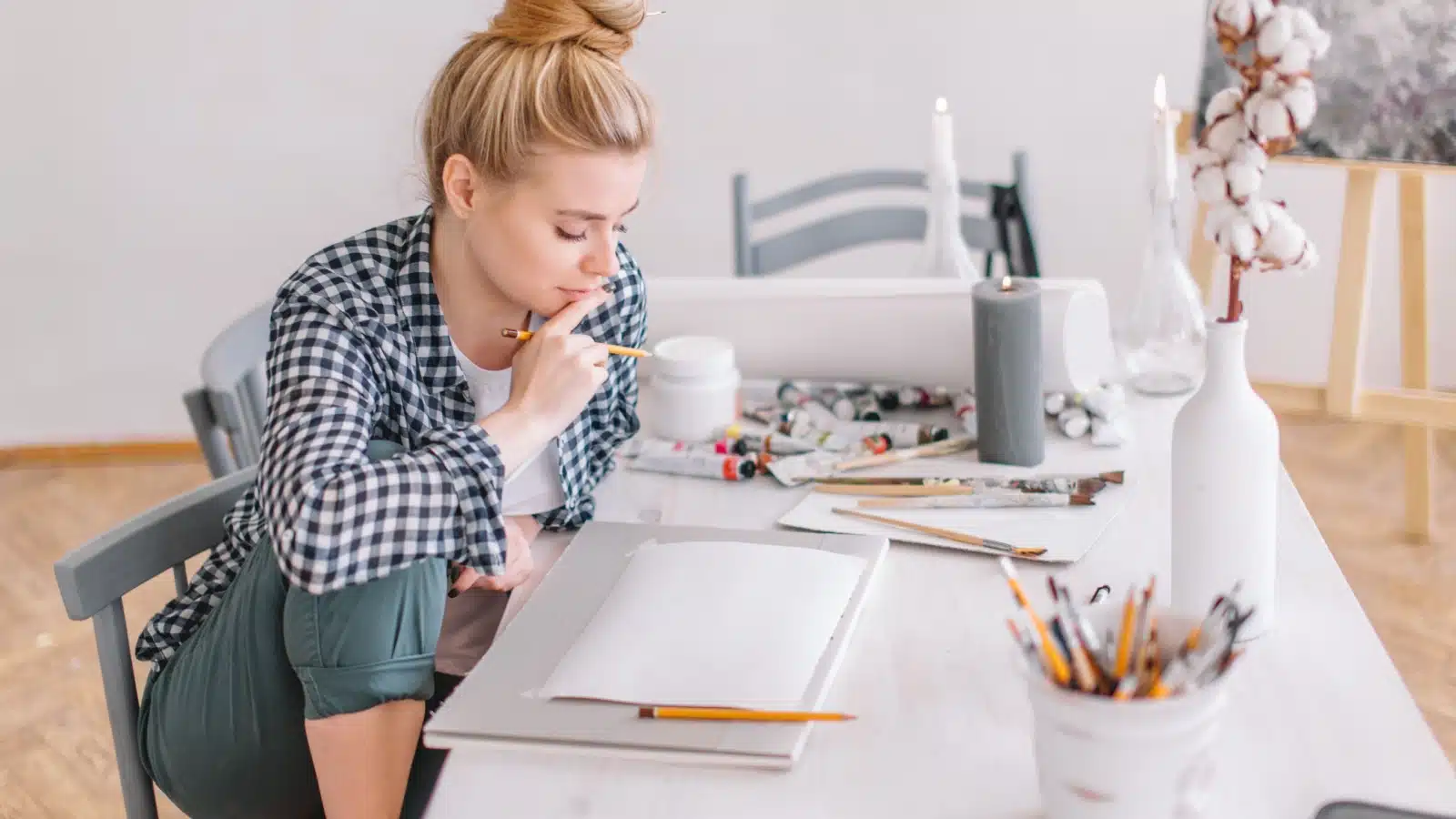 A woman with blank pages surrounded by art supplies wondering what to draw.