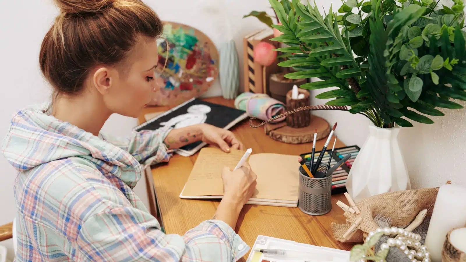 A woman writes in her journal, surrounded by art supplies, to represent art journal ideas.