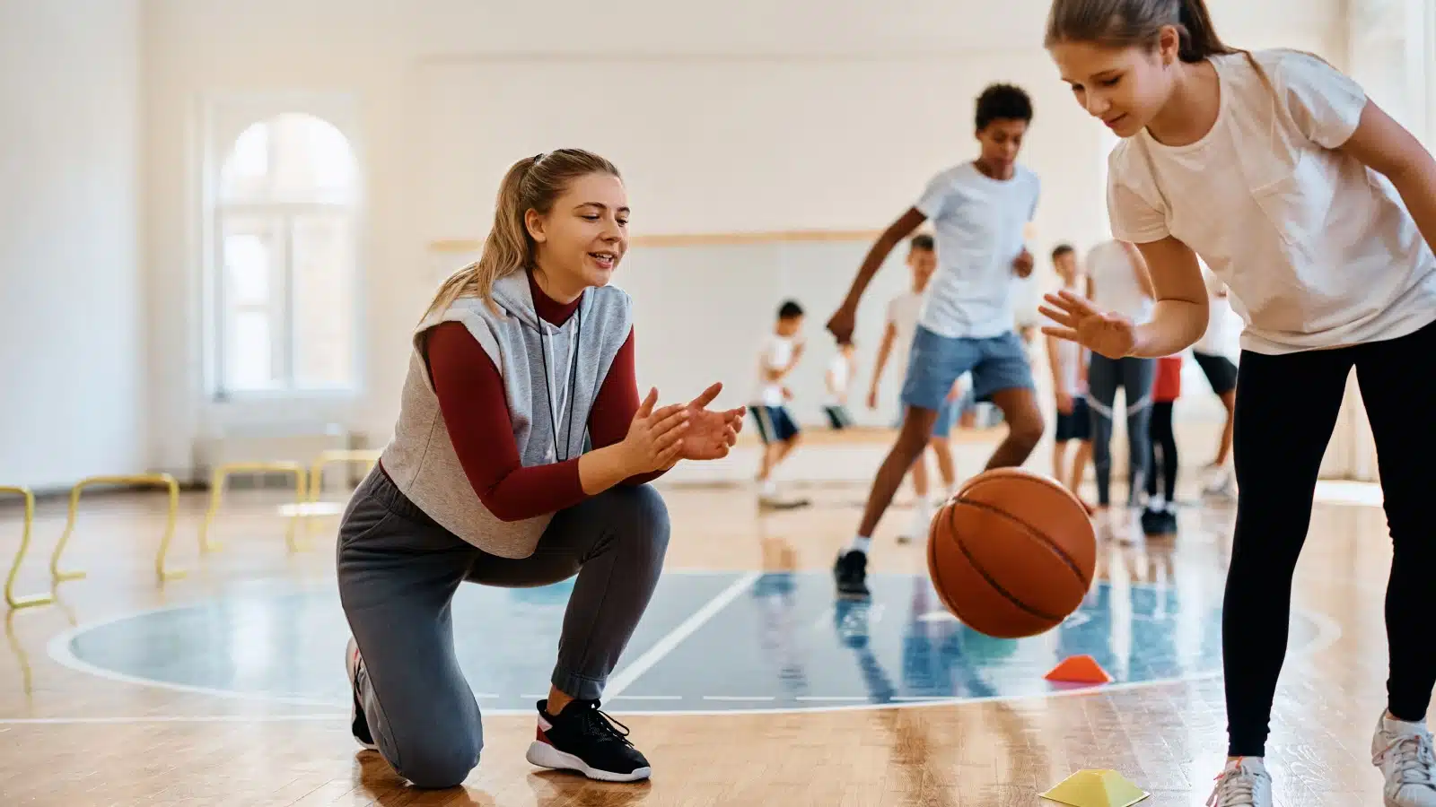 A coach helps a child practice dribbling a basketball. 