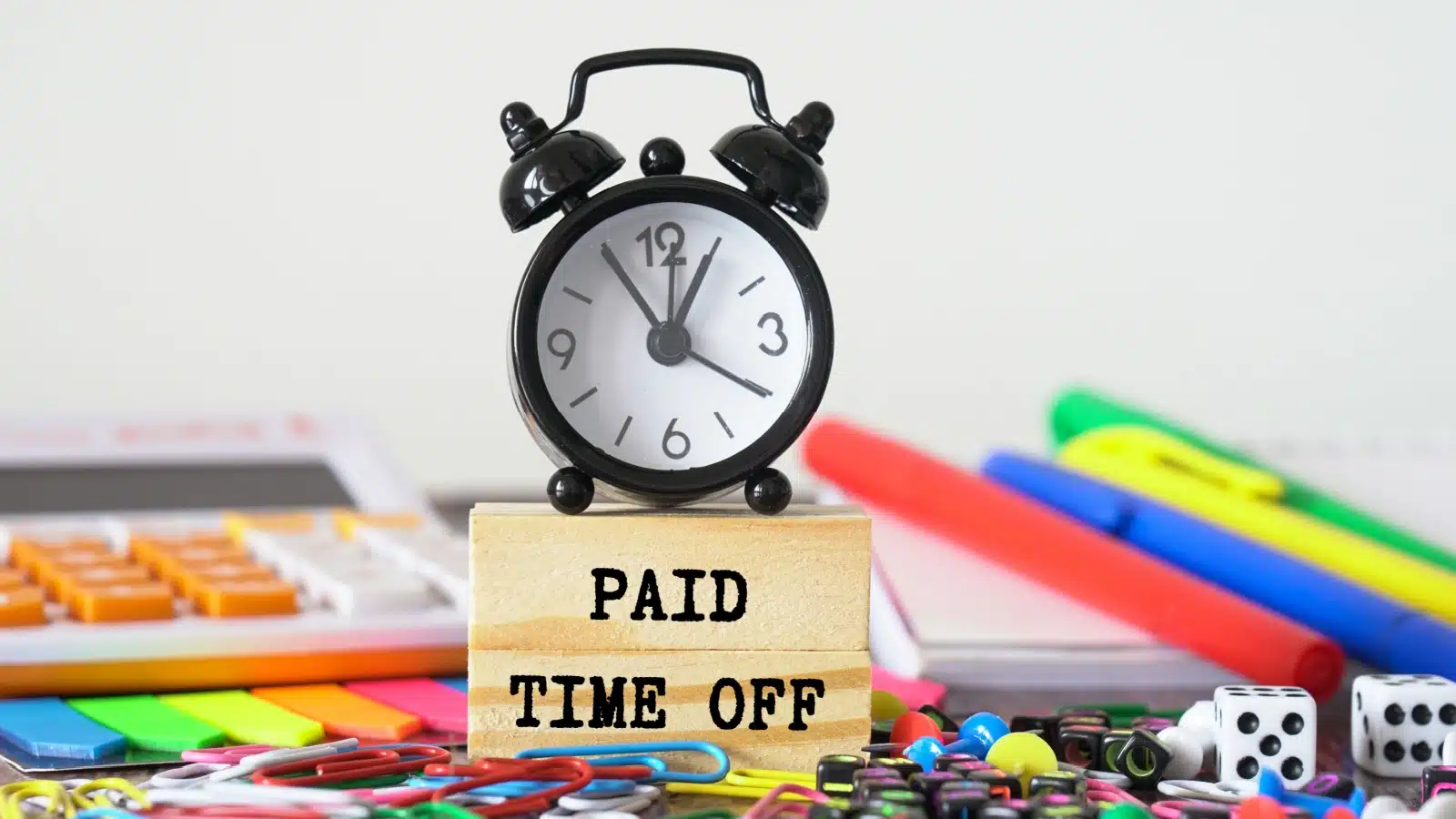 An alarm clock on a workspace sitting on block that says "paid time off."