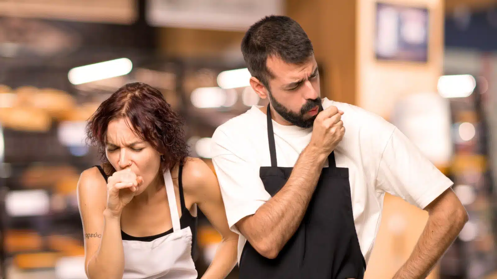 Sick servers coughing together at the restaurant where they work to illustrate how the lack of paid sick leave policies impact everyone.