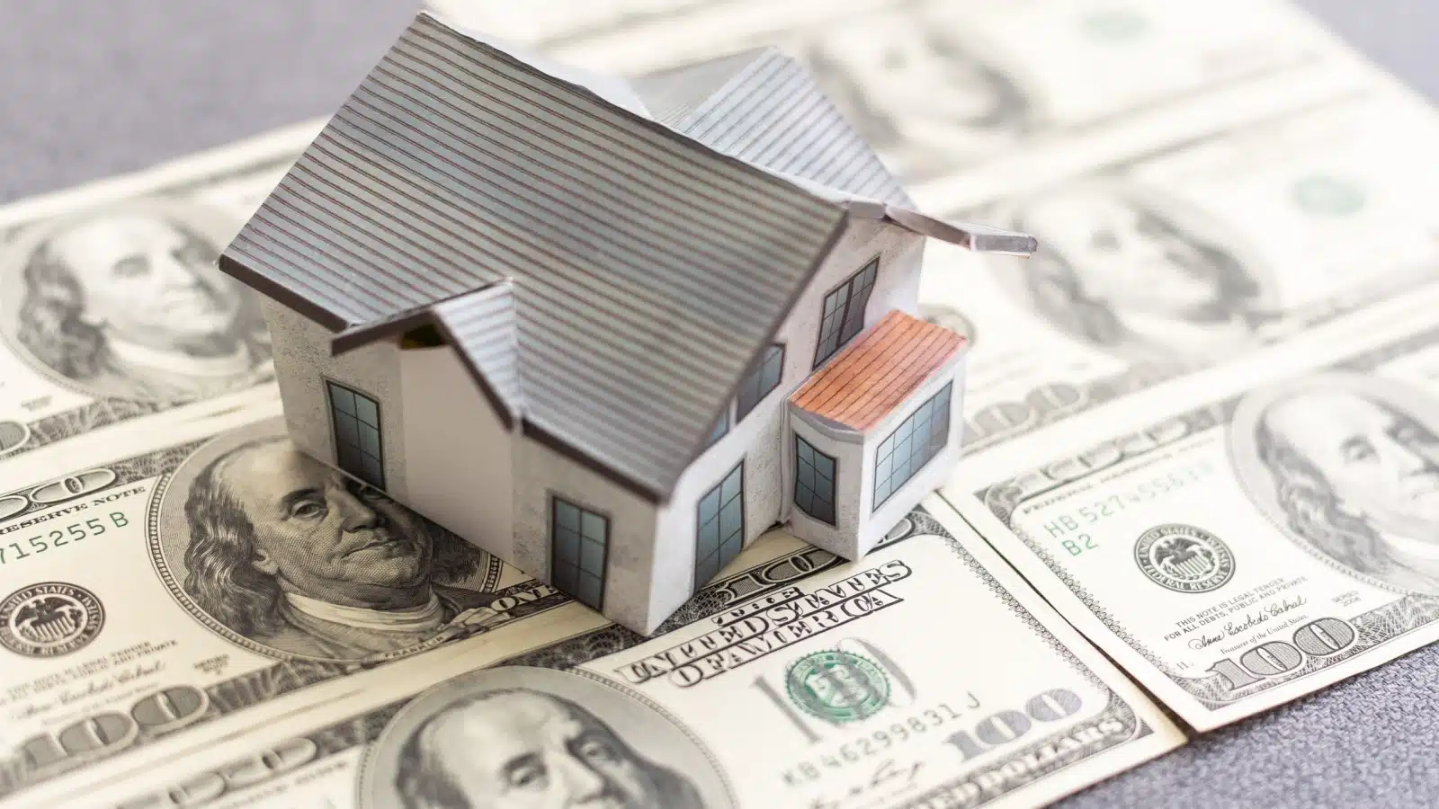 A miniature house sits atop a pile of hundred dollar bills to represent costly real estate mistakes. 