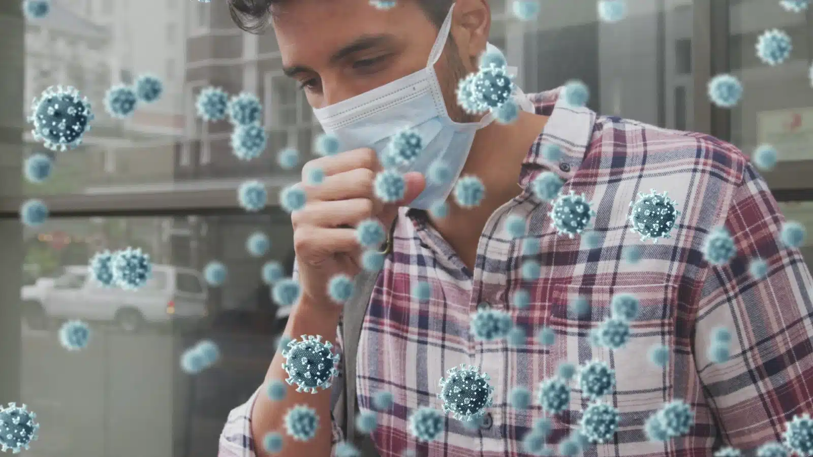 A man wearing a medical mask coughs. He's surrounded by large graphics representing germs.