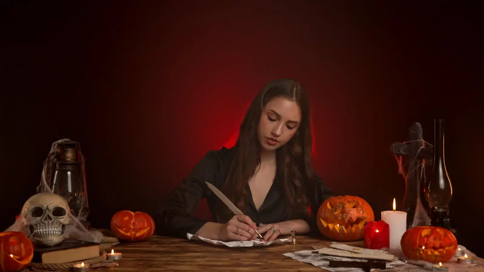 A gothic woman surrounded by red light and Halloween imagery writing a story.