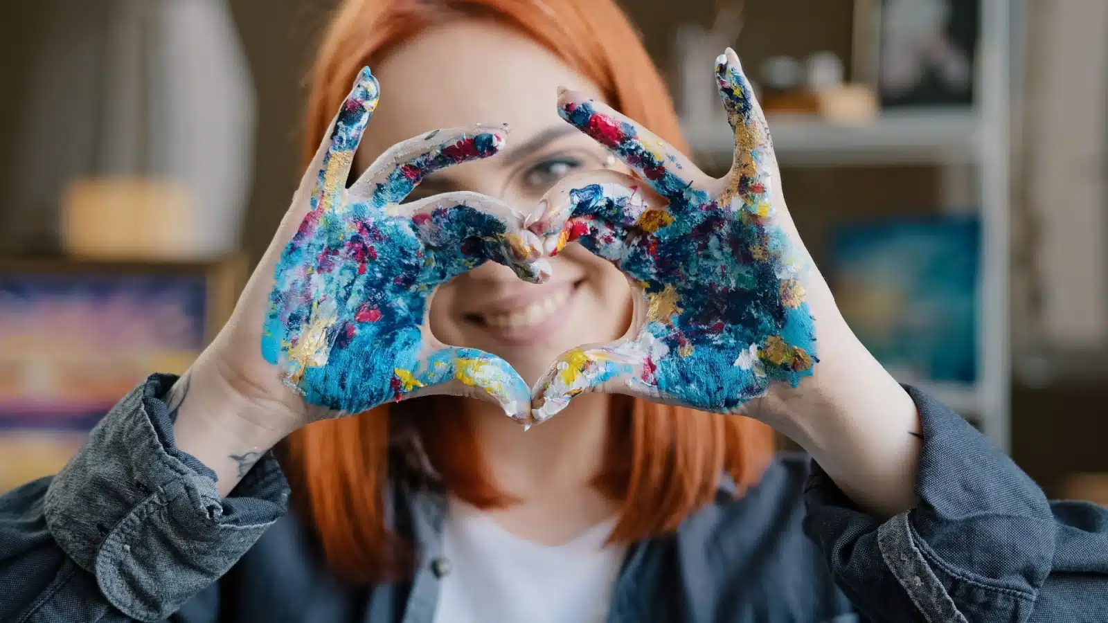 An artist with paint covered fingers making the thankfulness and gratitude sign with her hands.