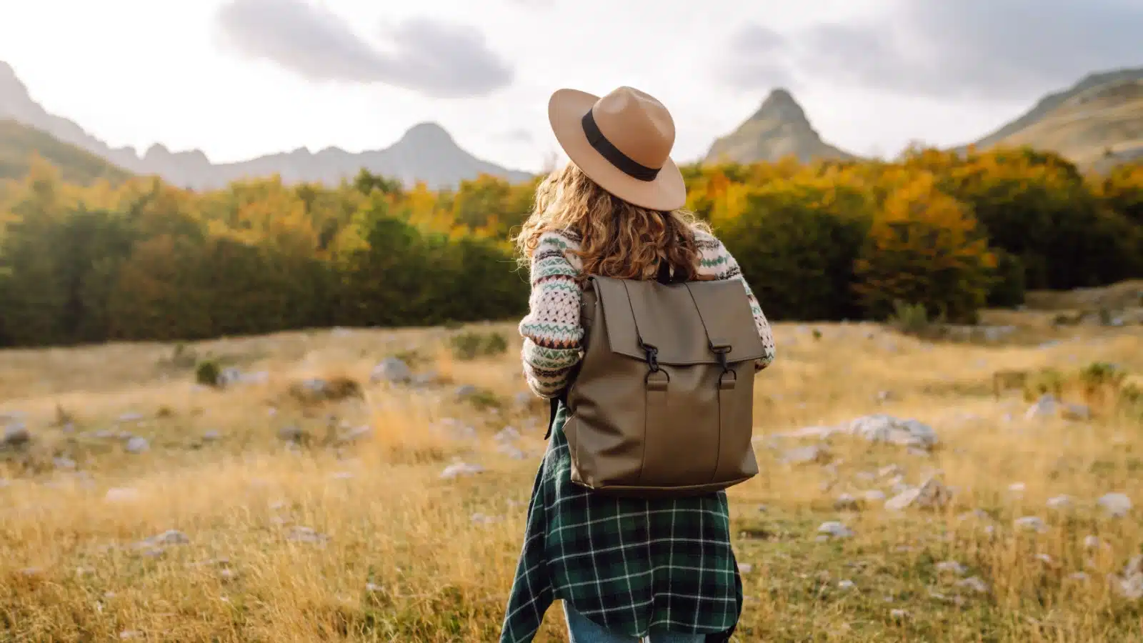 A woman backpacking alone in a field with mountains in the background to represent how to live an epic life.