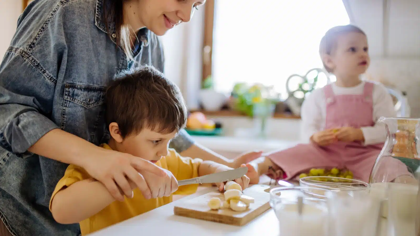 A mom helps her son slice bananas for breakfast.