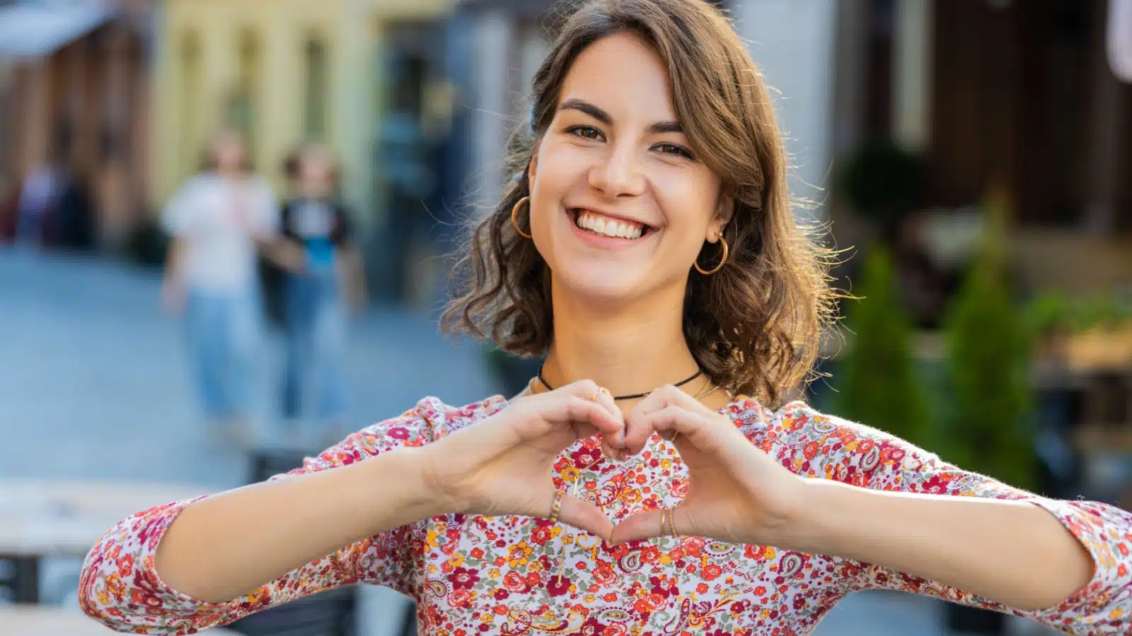 A smiling woman showing gratitude by making a heart symbol with her hands.