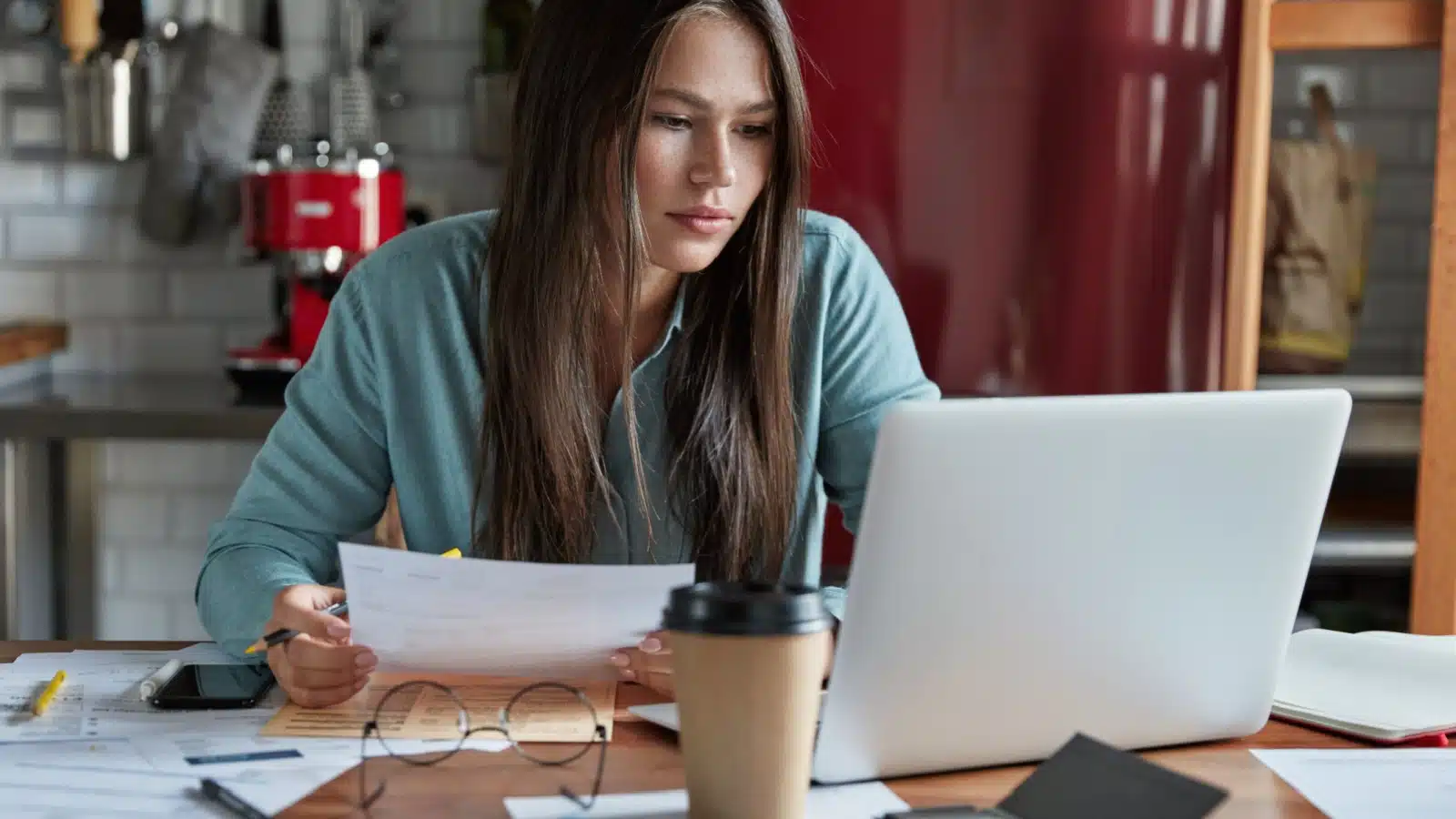 A woman reviews her bills and finances while working at her laptop. 