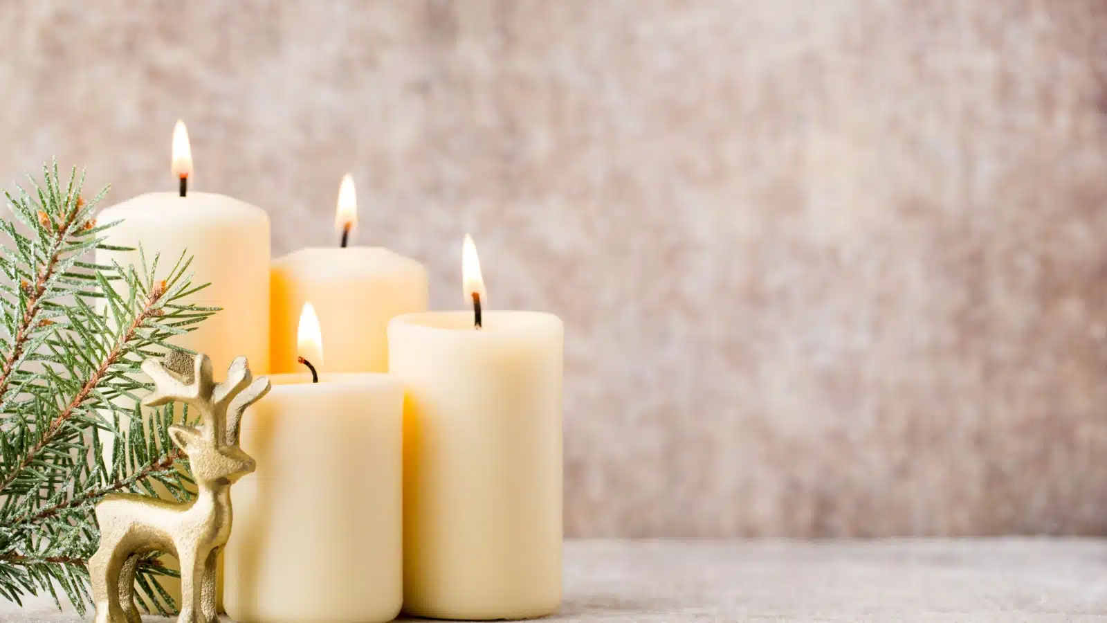 Four small white Christmas candles next to a small pine twig and a model reindeer.