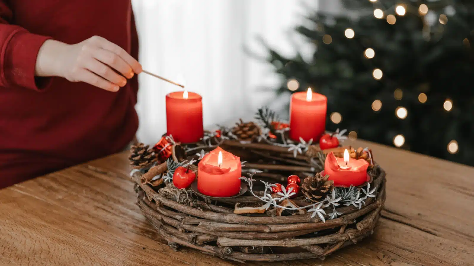A woman lights red scented candles resting on a wreath to make her home smell like Christmas.
