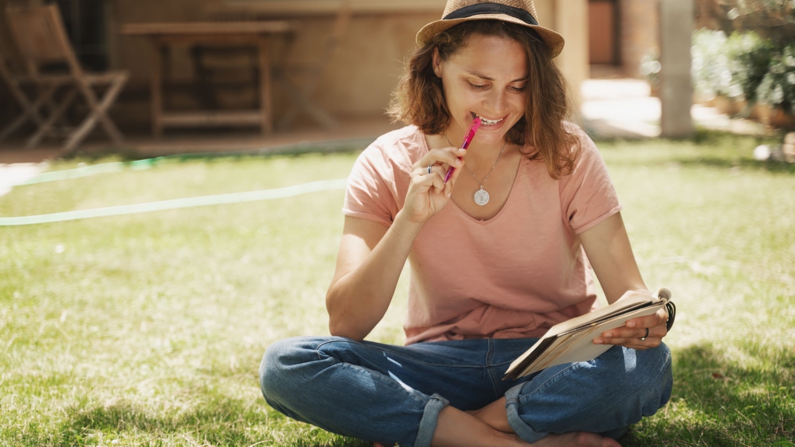 A happy, well adjusted woman sits outside in the grass writing in her journal, to represent the benefits of journaling for mental health.