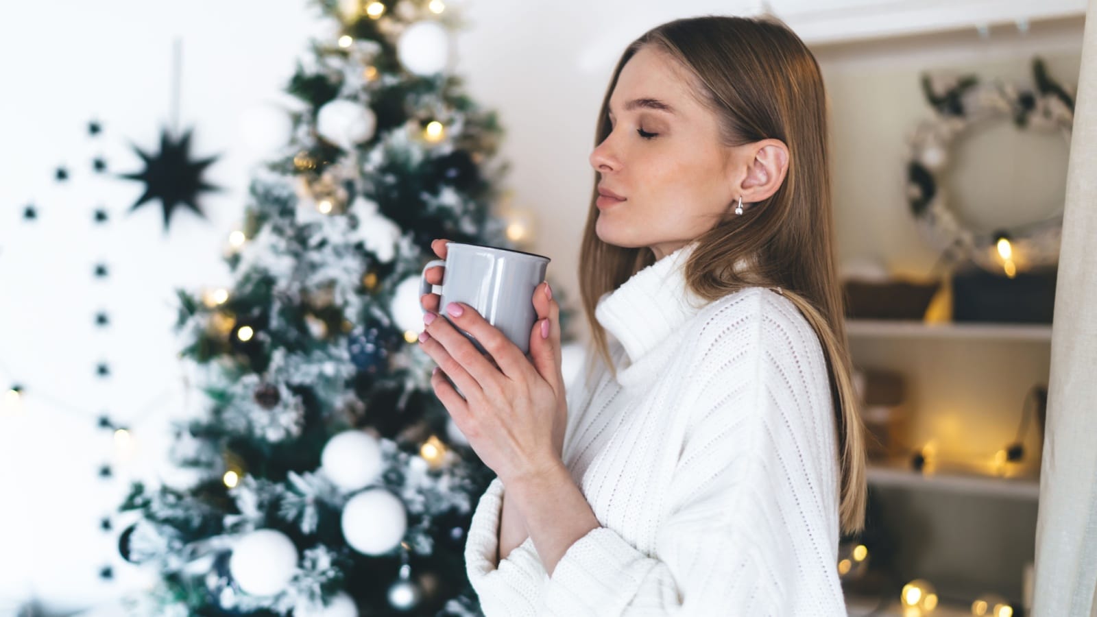A woman in front of a Christmas tree savors the smell of her hot cocoa to represent the best Christmas present smells.