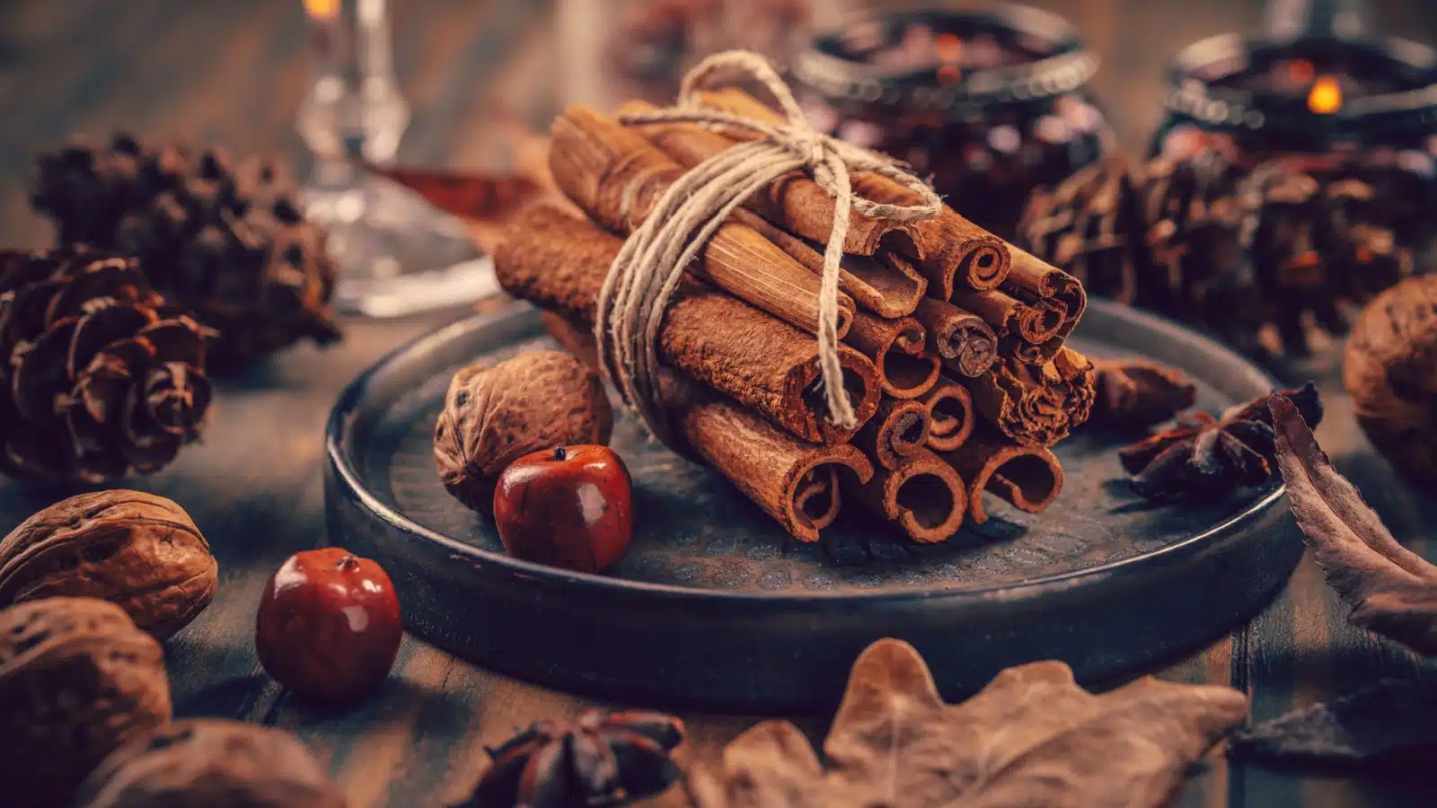 A bundle of cinnamon sticks on a table surrounded by nuts and pinecones.