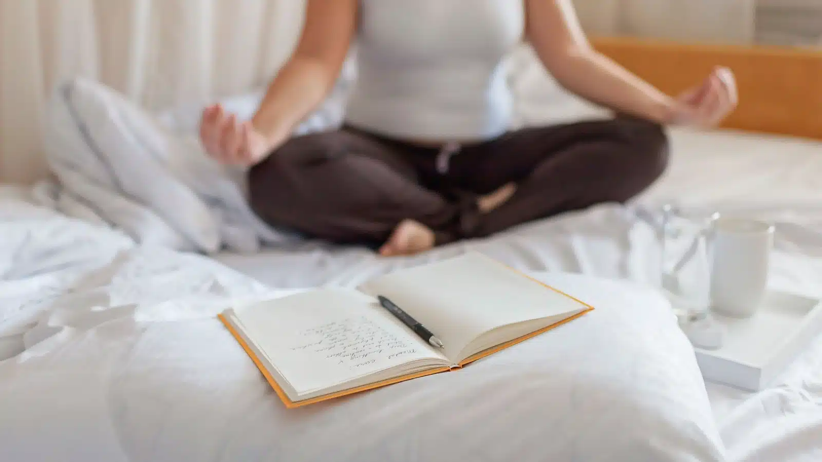 A woman meditates with a journal open in front of her, to represent journaling for wellness.