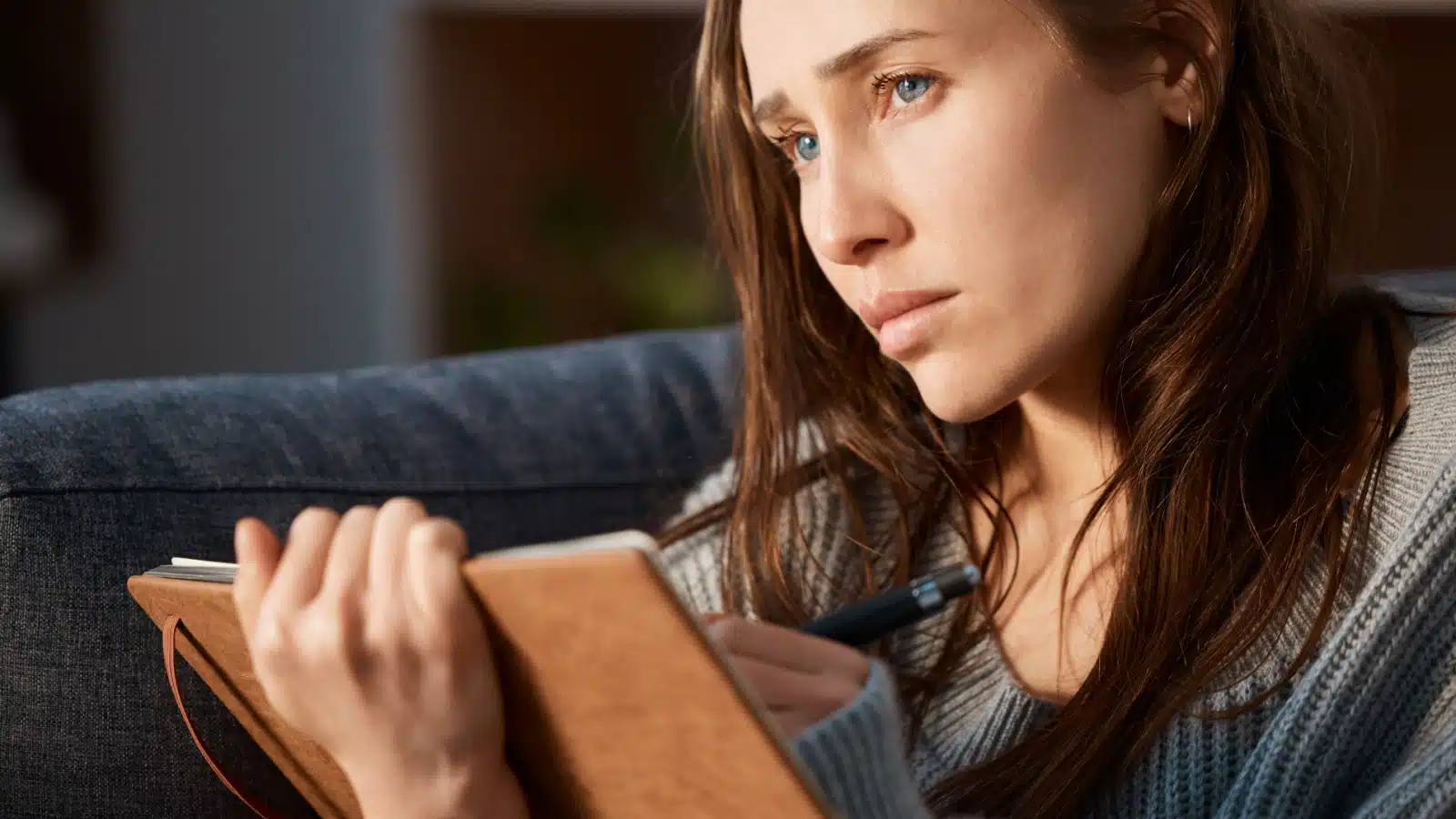 A sad woman writes in her journal, thinking about her issues, to represent journaling benefits.