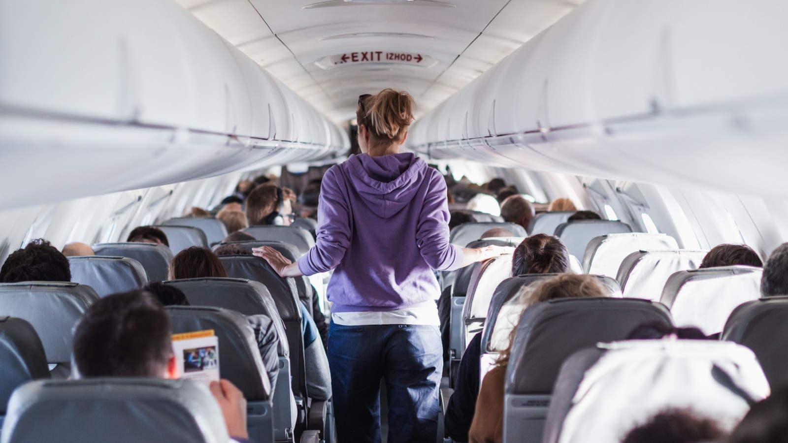 A passenger stretches her legs as she walks down the aisle of an airplane during a flight.