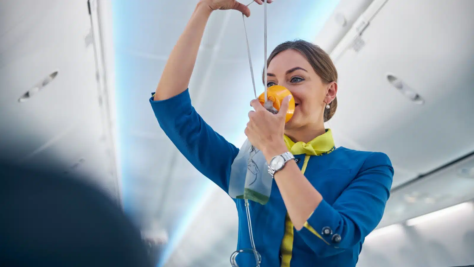 A flight attendant demonstrates how to put the oxygen mask on in an airplane.
