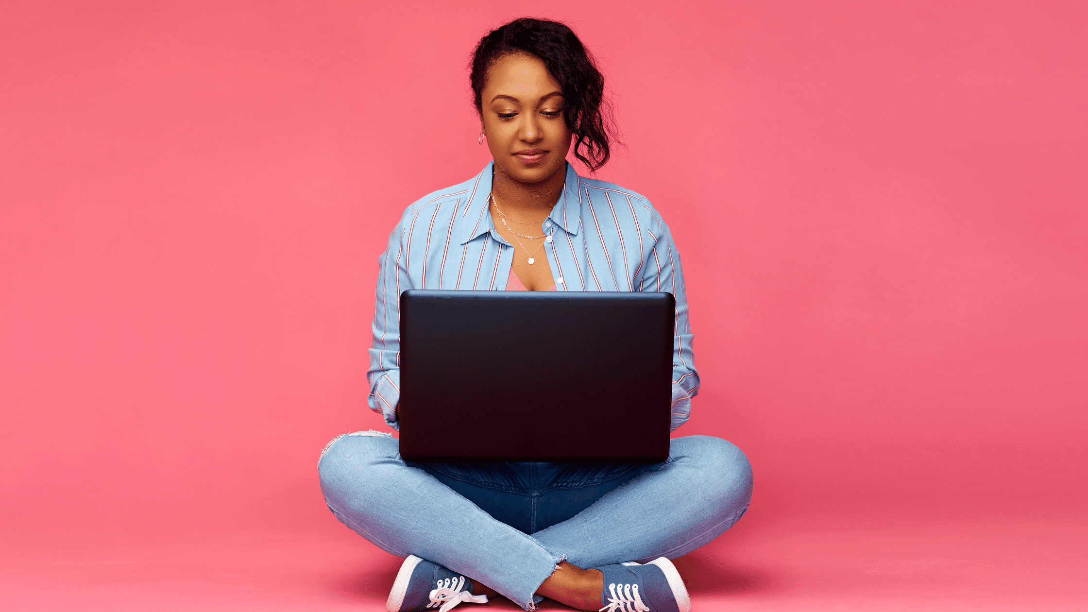woman using a laptop with a pink background
