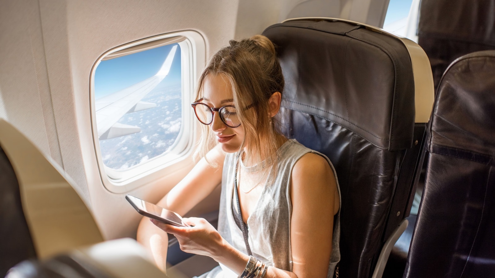 Have a safe Flight! A woman sits comfortably in a large airline seat, enjoying her flight while playing on her phone.