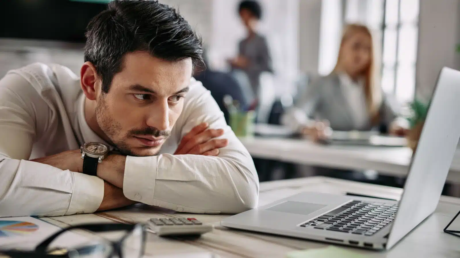 A tired office worker staring at his computer to represent the nine-to-five scam.
