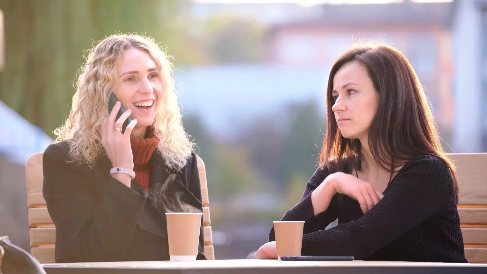 A woman happily talks on her cell phone while ignoring her friend. 