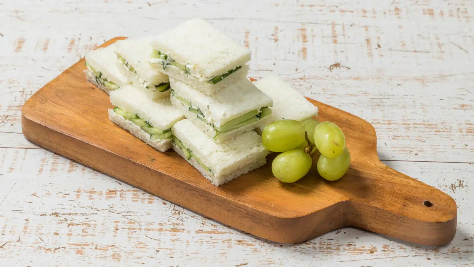 cucumber sandwiches with grapes on a cutting board.